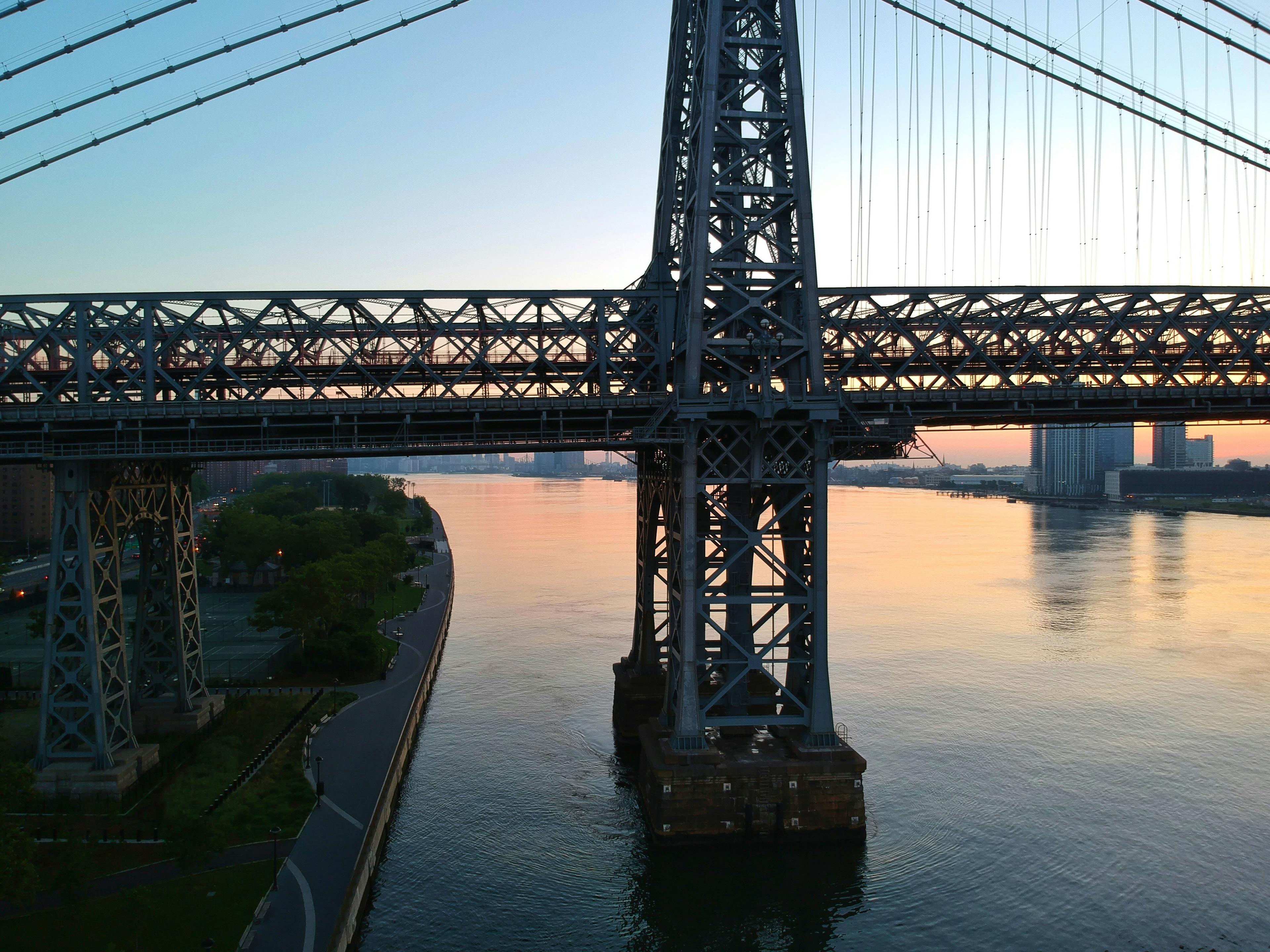 The Williamsburg Bridge viewed from beneath with the East River reflecting golden sunset light