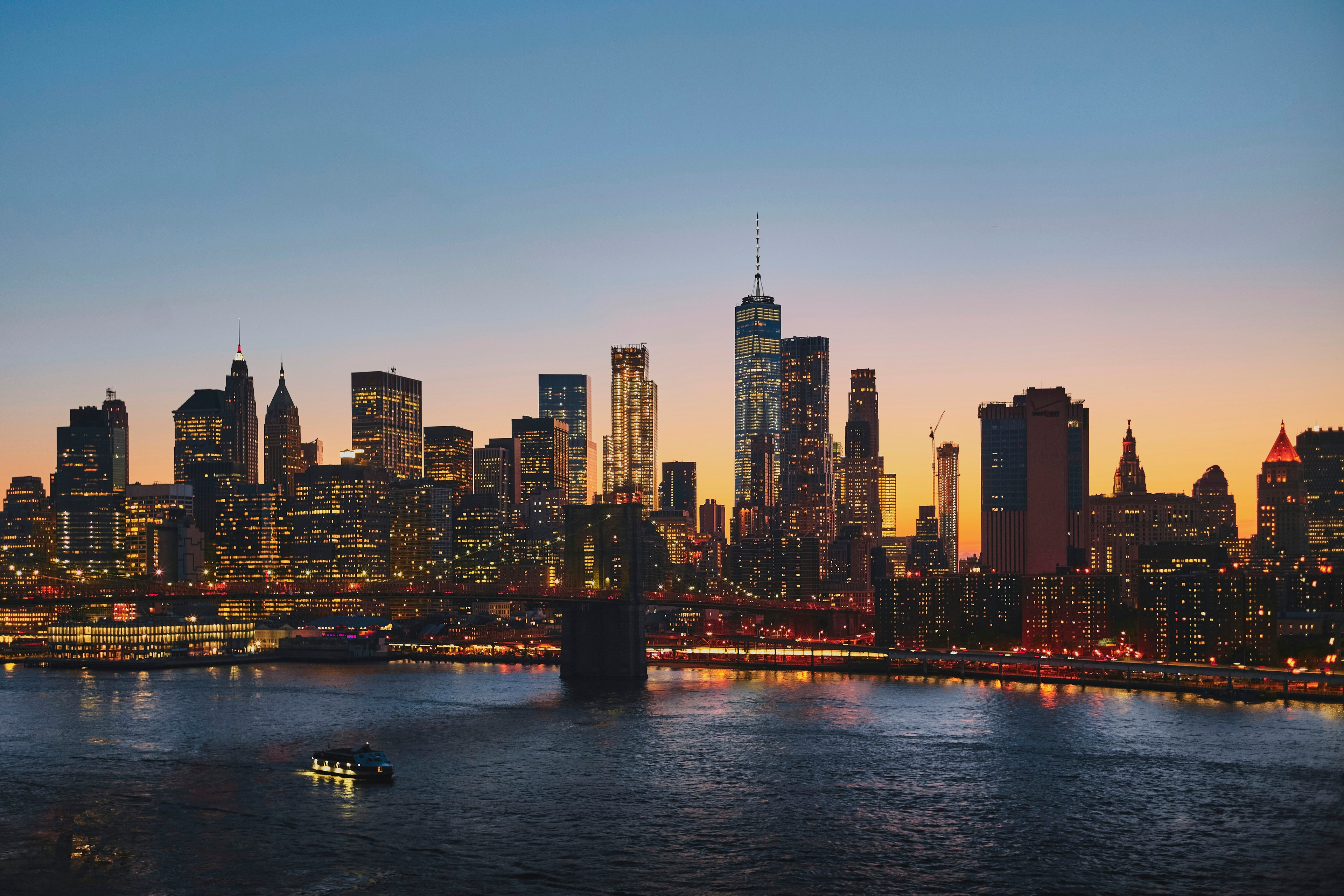 Manhattan skyline at golden hour seen from across the East River with the Brooklyn Bridge in the foreground