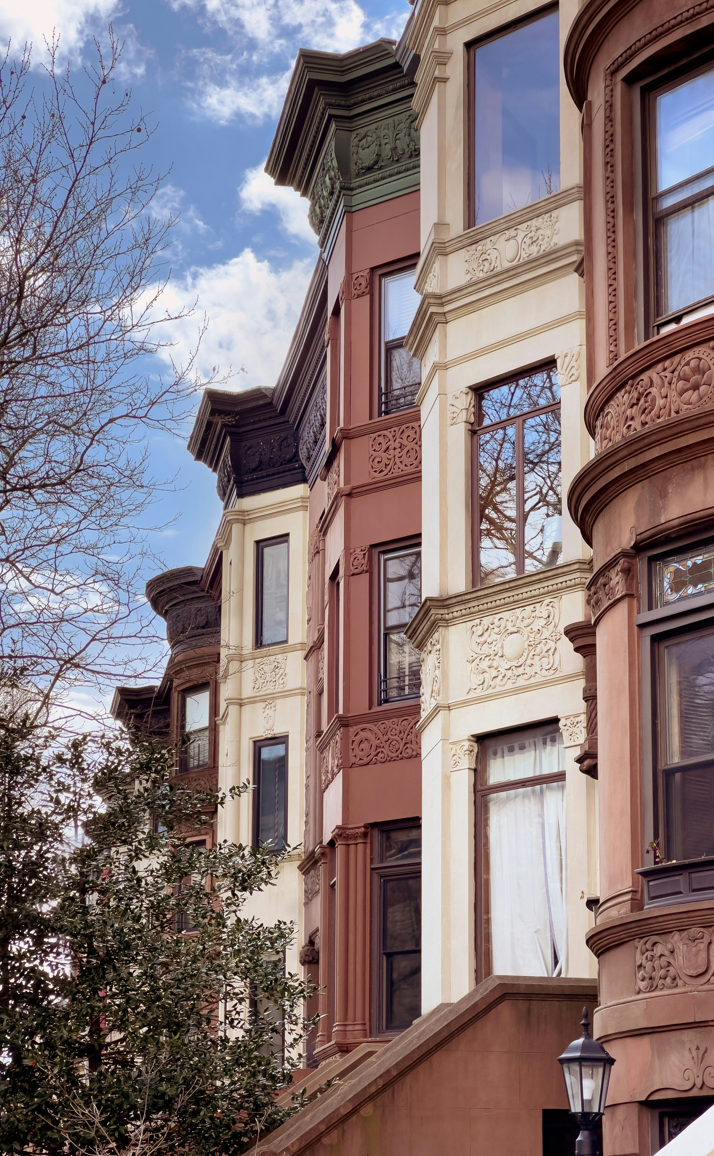 Park Slope brownstones with brown, cream, and terra-cotta facades against a partly cloudy sky